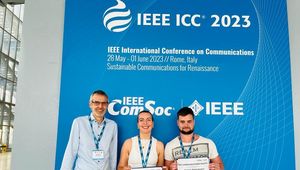 Picture with Andreas Springer and the two award winners Medina Hamidovic and Stefan Angerbauer in front of a blue backdrop with the writing "IEEE ICC 2023" on it