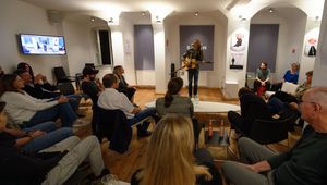 Veranstaltungsraum mit im Kreis sitzenden Publikum, Mann mit Gitarre steht vorne und singt