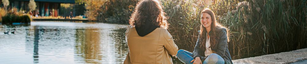 zwei Studentinnen sitzen am Teich vom JKU Campus