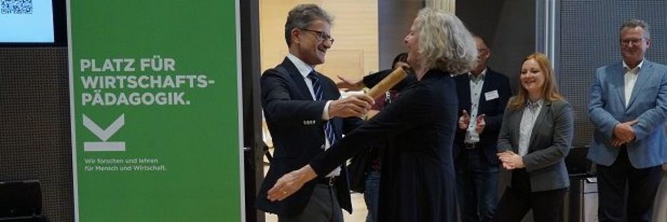 Prof. Neuweg hands the baton to Prof. Stock (University of Graz), hosts of the 2025 symposium; Photo credit: JKU
