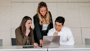 Drei Studierende blicken gemeinsam auf einen Laptop
