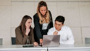 Three students look at a laptop together