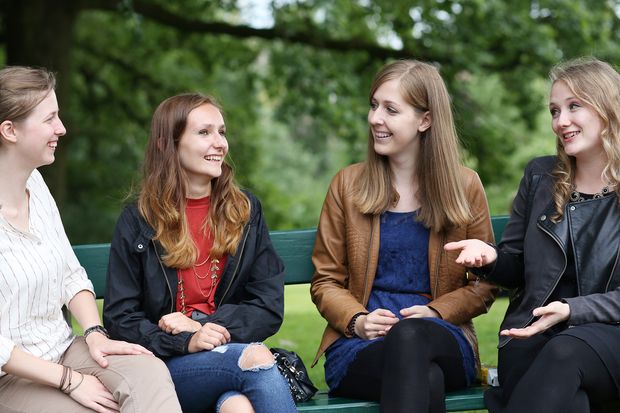vier lachende Studentinnen auf Parkbank sitzend