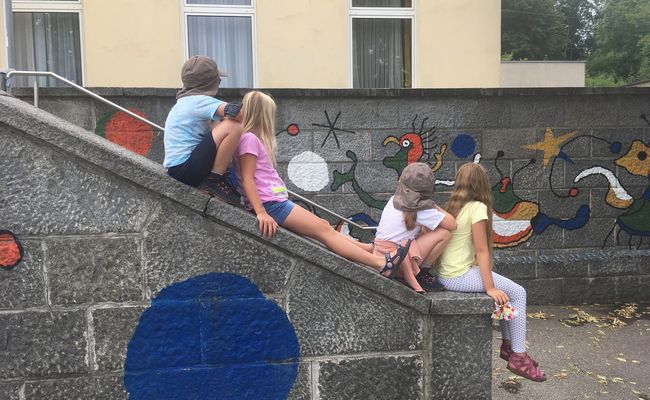 Foto von vier Kindern, die nebeneinander auf einer Mauer sitzen