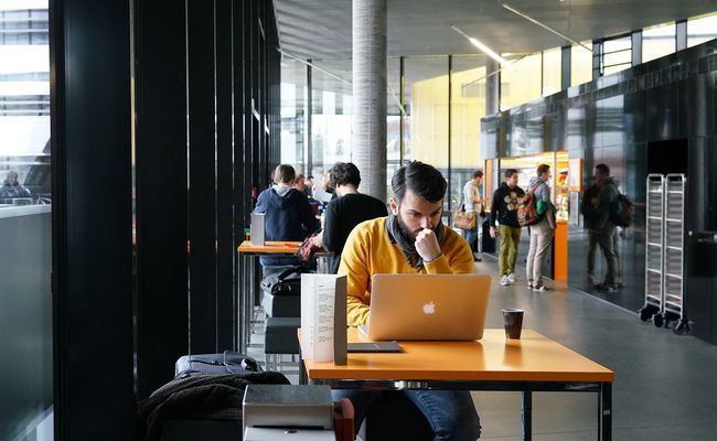 Studierender mit Notebook im Science Café sitzend, im Hintergrund weitere Gäste