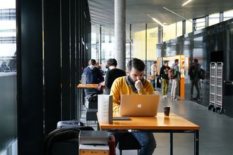 Studierender mit Notebook im Science Café sitzend, im Hintergrund weitere Gäste