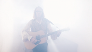 Mann mit Gitarre im erscheint hell angeleuchtet aus dem Nebel