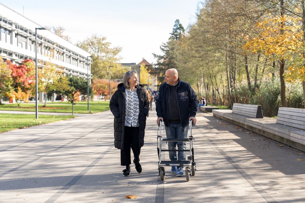 Zwei Menschen spazieren am Campus, einer davon mit Rollator
