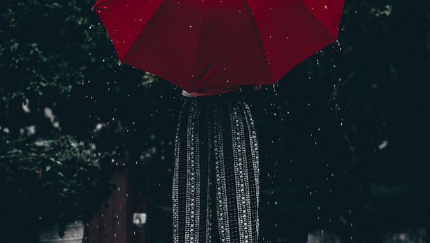 Rückansicht einer Frau mit rotem Regenschirm vor dunklem Hintergrund.