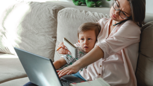 Frau arbeitet am Laptop und hält Kind umschlungen
