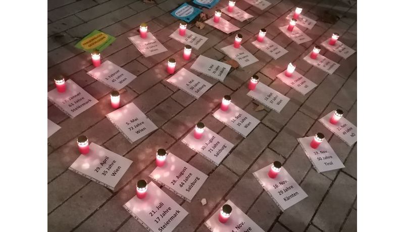 Die Demonstrant*innen legen 29 folierte A4-Blätter auf den Boden vor das Linzer Landhaus. Kerzen werden angezündet und je eine auf ein Blatt gestellt. Auf den Blättern stehen ein Datum, eine Altersangabe und ein österreichisches Bundesland. Die Kerzen stehen für die 29 Frauen die bereits im Jahr 2021 in Österreich von ihren Partnern oder Familienangehörigen ermordet wurden.