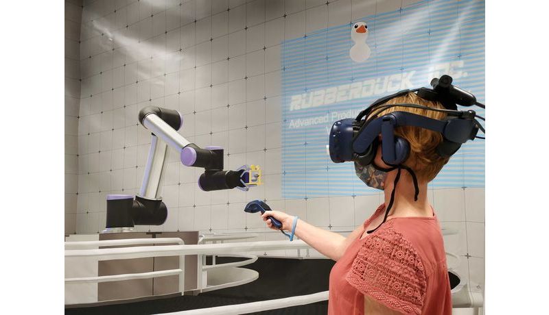 Person mit VR-Headset zeigt mit Controller auf Industrieroboterarm
