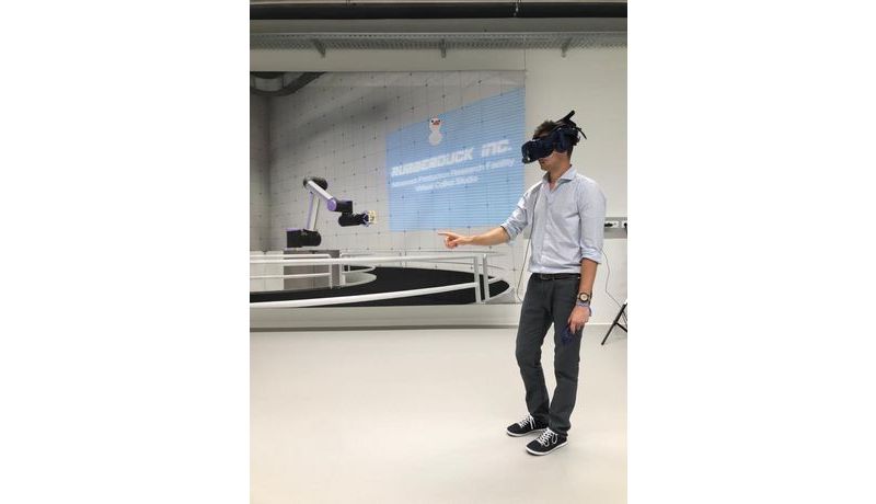 Person trägt VR-Headset, steht im Raum und tippt mit dem Finger in Richtung virtuellem Roboter