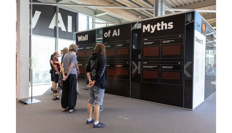 mehrere Personen stehen lesend vor einem Wandtext betitelt mit "Wall of AI Myths"