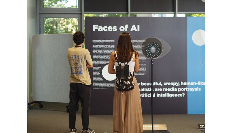 zwei Personen stehen vor einer Tafel mit einem Text betitelt "Faces of AI"