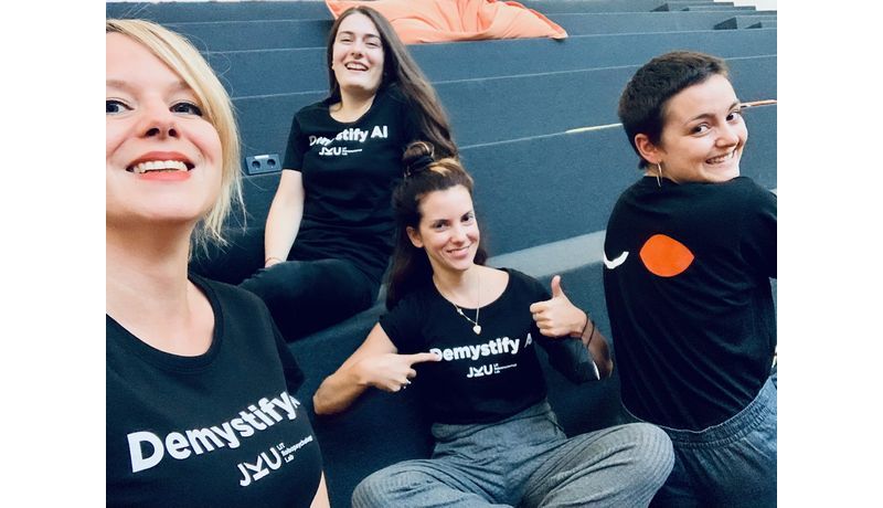 Vier Mitarbeiterinnen, die T-Shirts mit dem Logo des Labs und dem Schriftzug "Demystify AI" tragen.